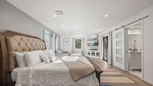 A modern bedroom with a large bed, a TV, and a bathroom with a vanity. - Large Private Backyard Oasis. Family Friendly - Arcade Room-5min to Down Town PS (Palm Springs)