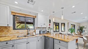 A modern kitchen with grey cabinets, a granite countertop, and a built-in dishwasher. - Large Private Backyard Oasis. Family Friendly - Arcade Room-5min to Down Town PS (Palm Springs)