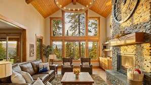 Un salón comedor espacioso con chimenea de piedra, muebles de cuero, ventanas amplias y techo de madera.