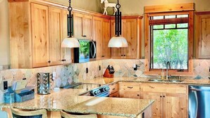 Une cuisine avec des meubles en bois, un plan de travail en granit, un four encastré et une fenêtre donnant sur un paysage verdoyant.