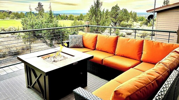 Un espace extérieur aménagé avec des sièges, une table avec foyer intégré et des coussins orange.
