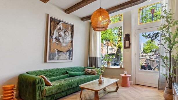 A green sofa, a wooden coffee table, and a hanging orange pendant light in a room with wooden floors and a large window.