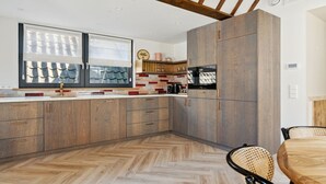 Eine moderne Küche mit Holzausstattung, einem Fischgrätparkett und einem Essbereich mit einem Korbtisch.