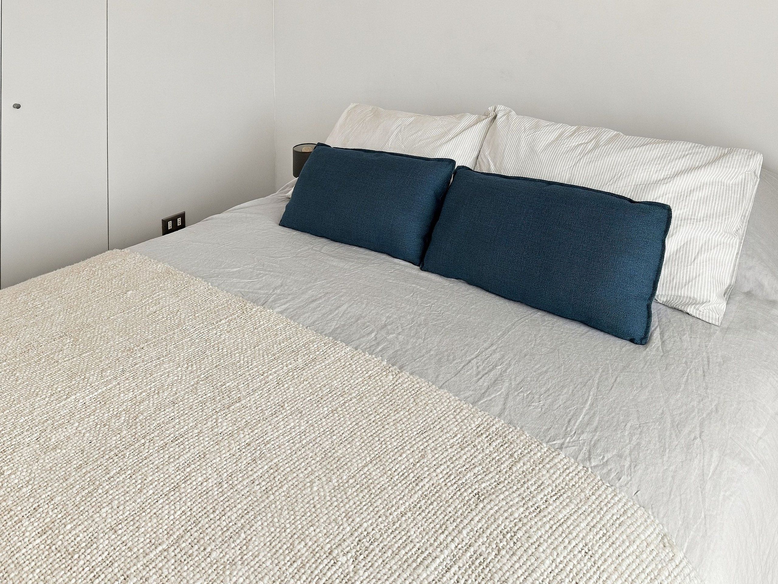 A bed with a textured bedspread and two pillows, one dark blue and one white striped.