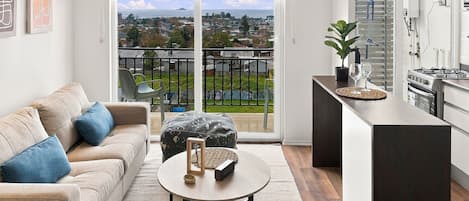 A modern apartment with a balcony, a kitchen, and a living area with a sofa and coffee table.