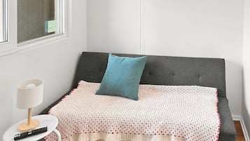 A small, cozy room with a grey sofa, a white lamp, and a remote control on a small table.