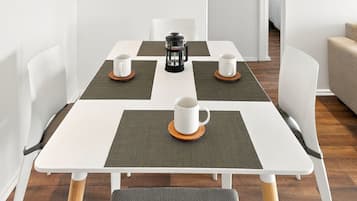 A modern dining area with a white table, four white cups, and a black coffee maker.