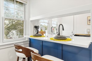 Une cuisine moderne dotée d’un grand îlot central, de meubles blancs et offrant une vue sur les arbres à l’extérieur.