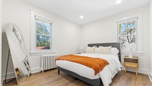 A bedroom with a bed, two windows, a radiator, and a bedside table. - The Bar Loft - Second Floor Suite. Close proximity to NYC and MetLife Stadium. (Bergenfield)