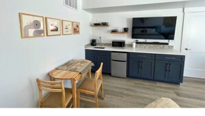 Une cuisine moderne avec des meubles de couleur sombre, une table à manger en bois et un téléviseur à écran plat.