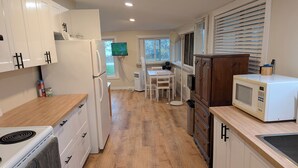 A modern kitchen with white cabinets, a microwave, a stove, and a dining area with a table and chairs. - South Shore Cottage With Lake View (Pelee)