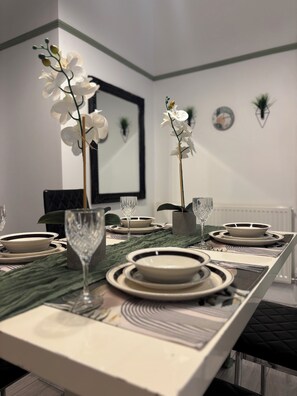 Une table à manger dressée avec des assiettes, des bols et des verres, agrémentée de vases contenant des orchidées.