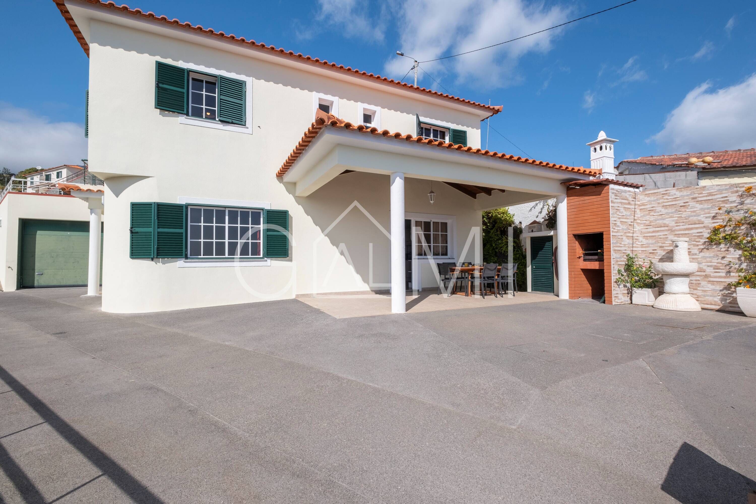 A two-story house with a covered patio, a garage, and a stone wall.