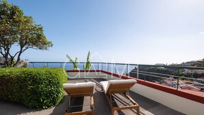 Un balcon avec deux fauteuils de jardin en bois, une vue sur la mer et une rambarde rouge.