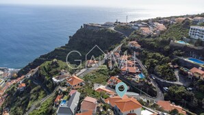 Vue aérienne d’un quartier résidentiel situé sur la côte, avec des maisons, une route sinueuse et une falaise surplombant la mer.