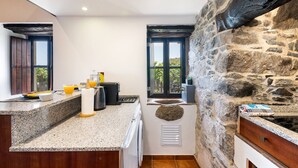Une cuisine dotée de plans de travail en granit, d’un mur en pierre et d’une fenêtre donnant sur un paysage verdoyant.