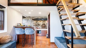 Un espace de vie compact comprenant une chambre en mezzanine, un coin cuisine et un escalier.