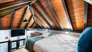 Une chambre avec un plafond en pente, un lit, une table de chevet, une télévision et un petit coin salon.