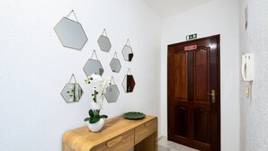 A wooden console table with a vase of flowers and a green plate, a wooden door with a sign, and hexagonal mirrors on the wall.