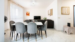 A dining area with a white table and grey chairs, a black sofa, and a small side table with a speaker.