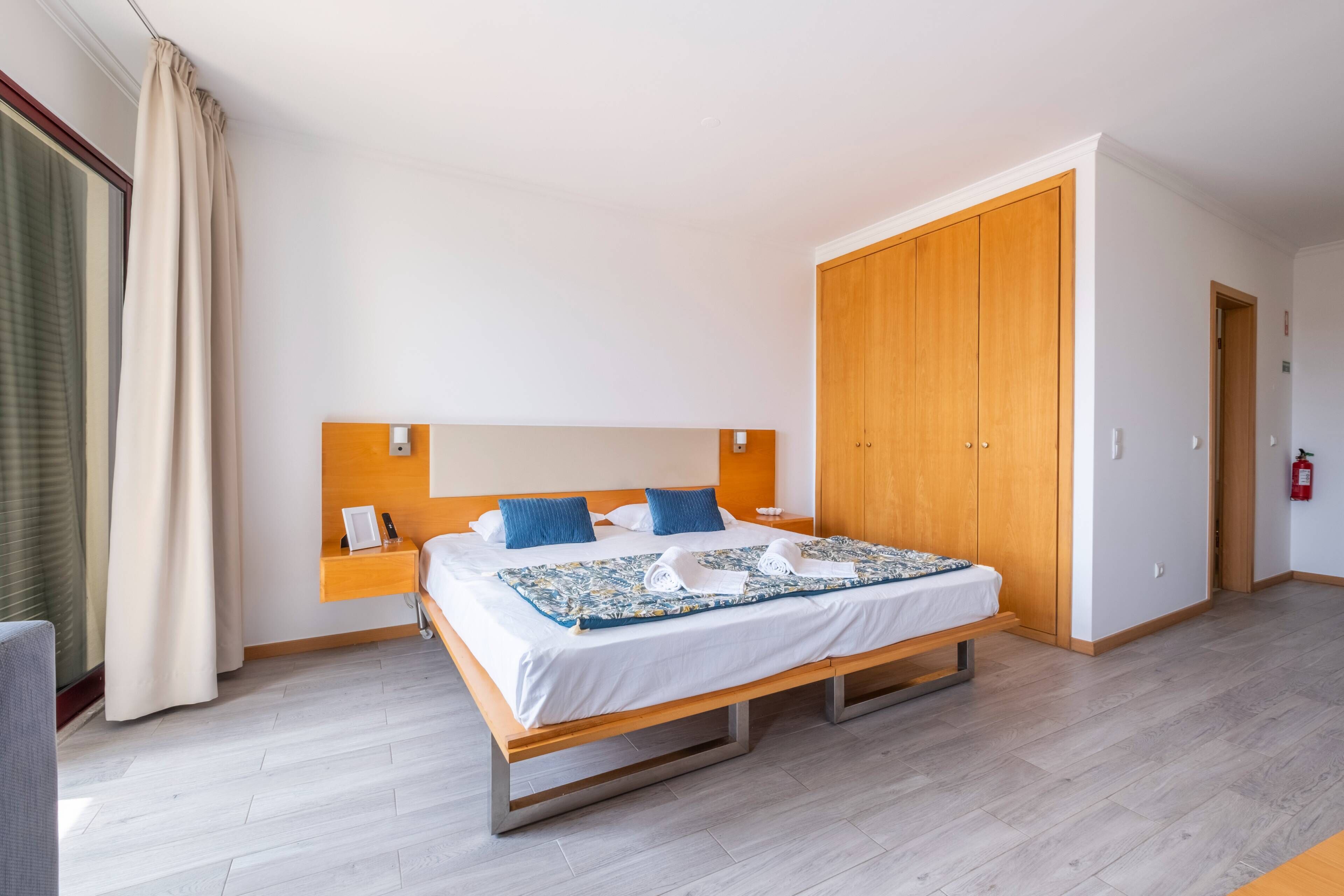 Habitació d'hotel amb un llit, un armari de fusta i una tauleta de nit amb un telèfon i una làmpada.