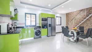 A modern kitchen with green cabinets, a built-in washing machine, and a dining area with a glass table and chairs. - Shell House by GALMI (Calheta (Madeira))