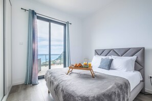 A modern bedroom with a large bed, a breakfast tray, and a balcony with a view. - Shell House by GALMI (Calheta (Madeira))
