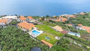 An aerial view of a residential area with houses, a swimming pool, and a large body of water in the background. - Shell House by GALMI (Calheta (Madeira))