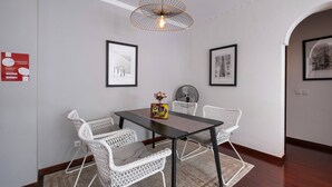 A dining area with a table and four white chairs, a hanging light fixture, and framed pictures on the walls. - Stylish Garden Apartment by GALMI (Santa Cruz)