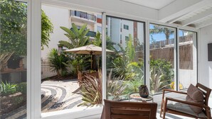 A sunlit patio with a wooden table and chairs, surrounded by lush plants and a small garden. - Stylish Garden Apartment by GALMI (Santa Cruz)