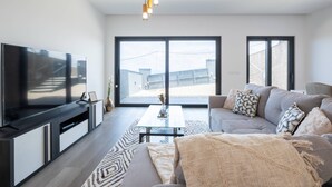 A modern living room with a flat-screen TV, a sofa, a coffee table, and a large window offering a view of buildings. - Villa Bela Horizonte by GALMI (Santa Cruz)