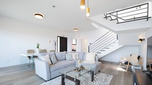 A modern living room with a grey sofa, glass coffee table, and a staircase with a metal railing. - Villa Bela Horizonte by GALMI (Santa Cruz)