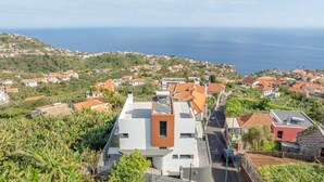 A coastal residential area with modern houses, a clear view of the sea, and a road leading to a building with a flat roof and a water tank. - Villa Oceano Sereno by galmi (Ponta do Sol)
