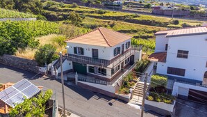 A two-story house with a balcony, surrounded by greenery and a road. - Villa Pequenino by GALMI (Calheta (Madeira))