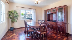 A dining room with a wooden table and chairs, a potted plant, and a cabinet with glass doors. - Villa Pequenino by GALMI (Calheta (Madeira))