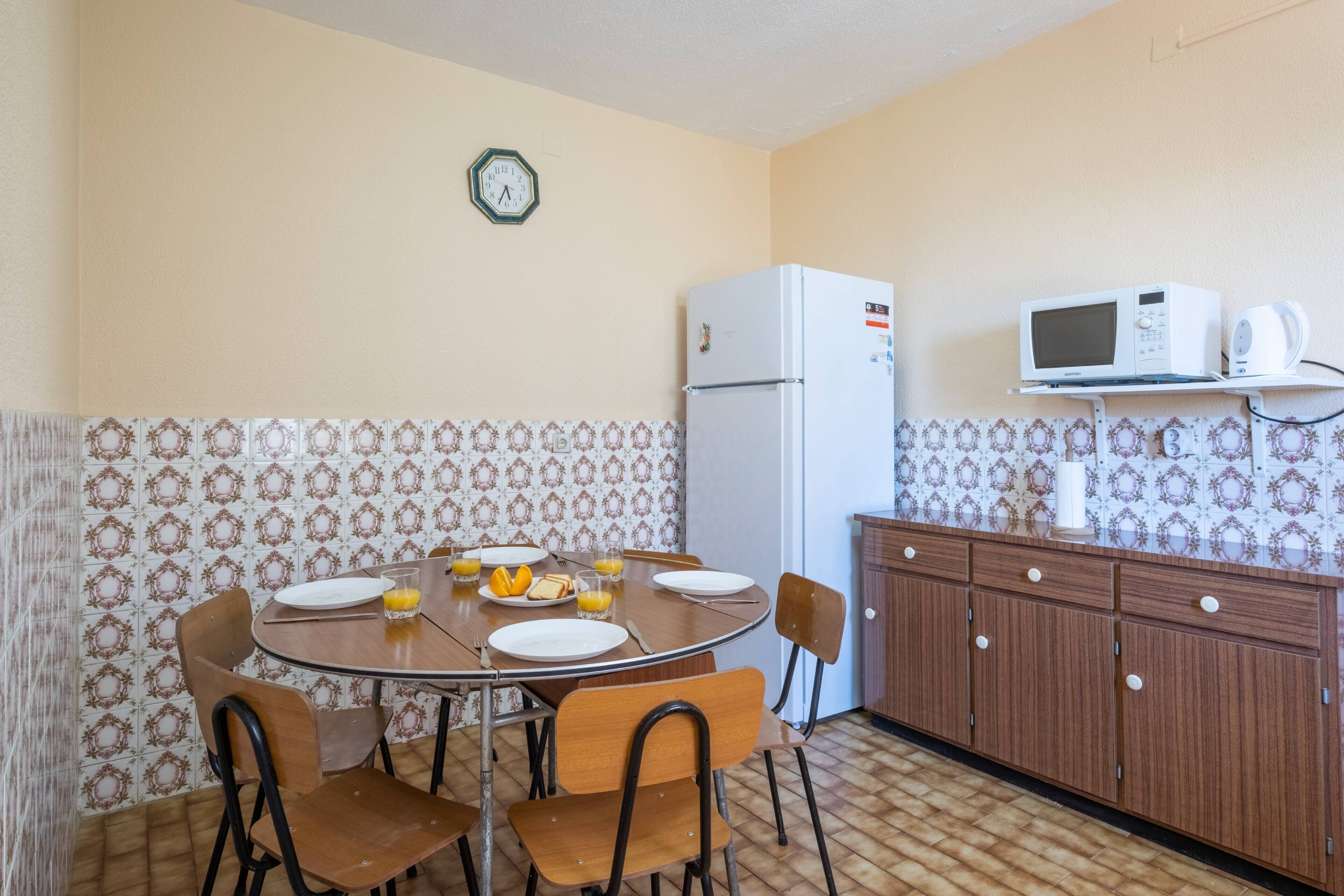 A compact kitchen with a dining table set for four, a refrigerator, a microwave, and a cabinet with a patterned backsplash.