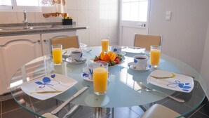 Ein Frühstückstisch mit Orangensaft, Kaffee und Obst in einem hellen Raum mit weißen Wänden und einem Fenster.