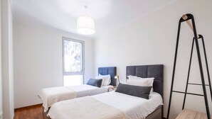 Una habitación con dos camas, una ventana, una lámpara de pie y una escalera de madera.