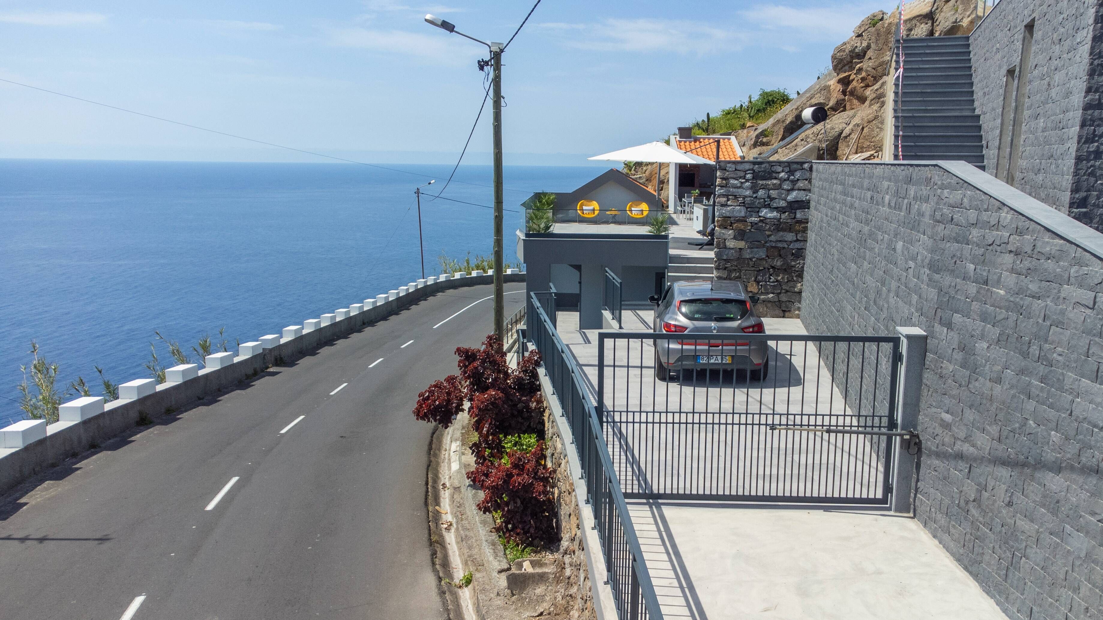 Une route côtière avec une voiture garée dans une zone délimitée par des barrières, d’où l’on a une vue sur la mer.