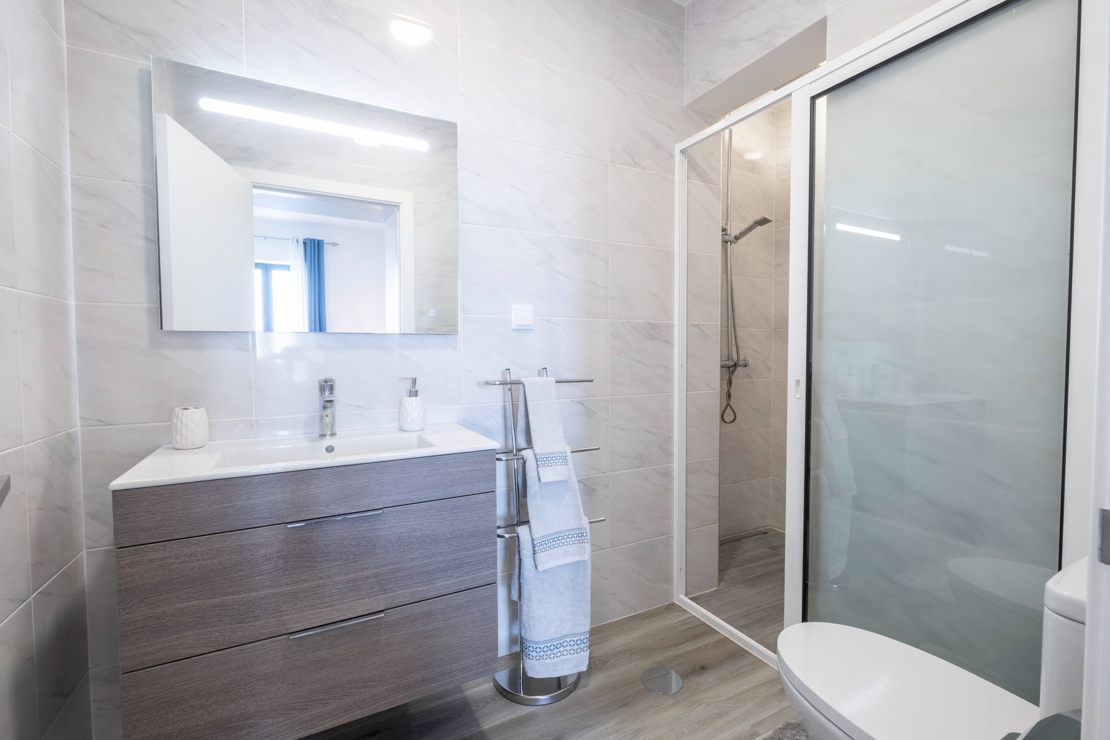 A modern bathroom with a large mirror, a vanity with drawers, a glass shower enclosure, and a toilet.