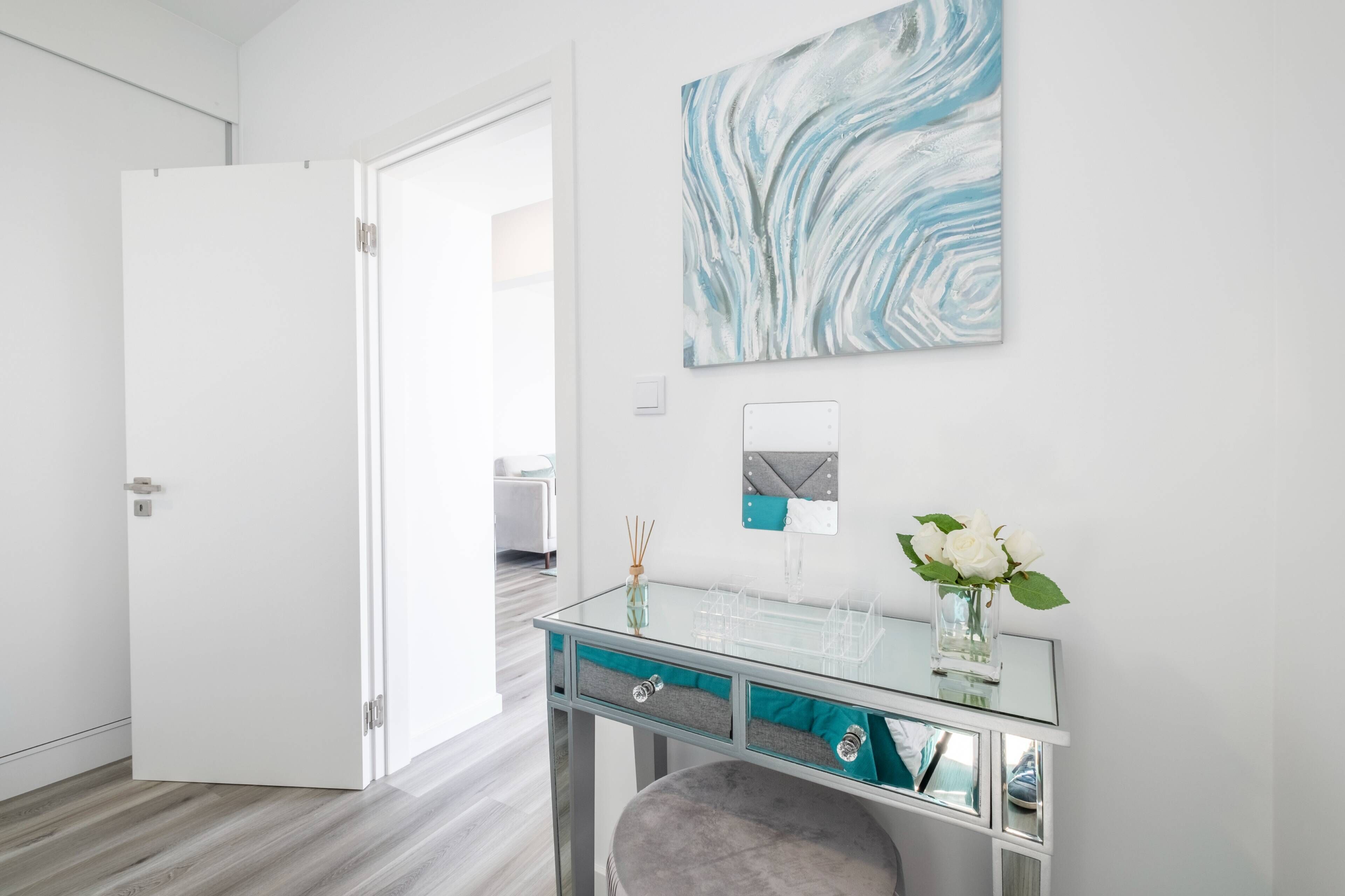 A modern bathroom with a glass vanity, a white door, and a wall-mounted artwork.