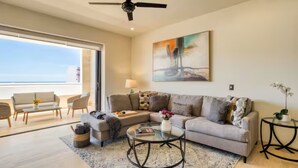 A spacious living room with a large sofa, a coffee table, and a view of the ocean through a sliding glass door. - Your perfect family getaway: relax between the pool, the jacuzzi and the sea. (San José del Cabo)