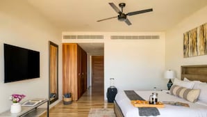 A hotel room with a bed, a TV, a ceiling fan, a wooden wardrobe, a suitcase, and a painting on the wall. - Your perfect family getaway: relax between the pool, the jacuzzi and the sea. (San José del Cabo)