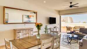 A dining area with a wooden table and chairs, a vase with flowers, a flat-screen TV on the wall, and a view of the sea through large windows. - Your perfect family getaway: relax between the pool, the jacuzzi and the sea. (San José del Cabo)