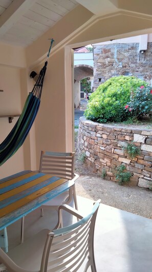 A patio with a hammock, a table, and chairs. There is a stone wall with greenery and a building in the background. - Ligurian village, apartment in the historic center (Diano Marina)