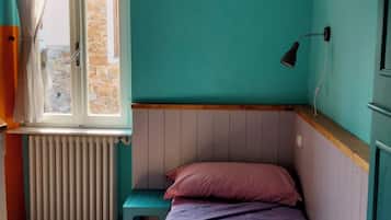 Een kleine kamer met een enkel bed, teal muren, een houten hoofdbord, een raam met gordijnen, een radiator en een bedlampje.