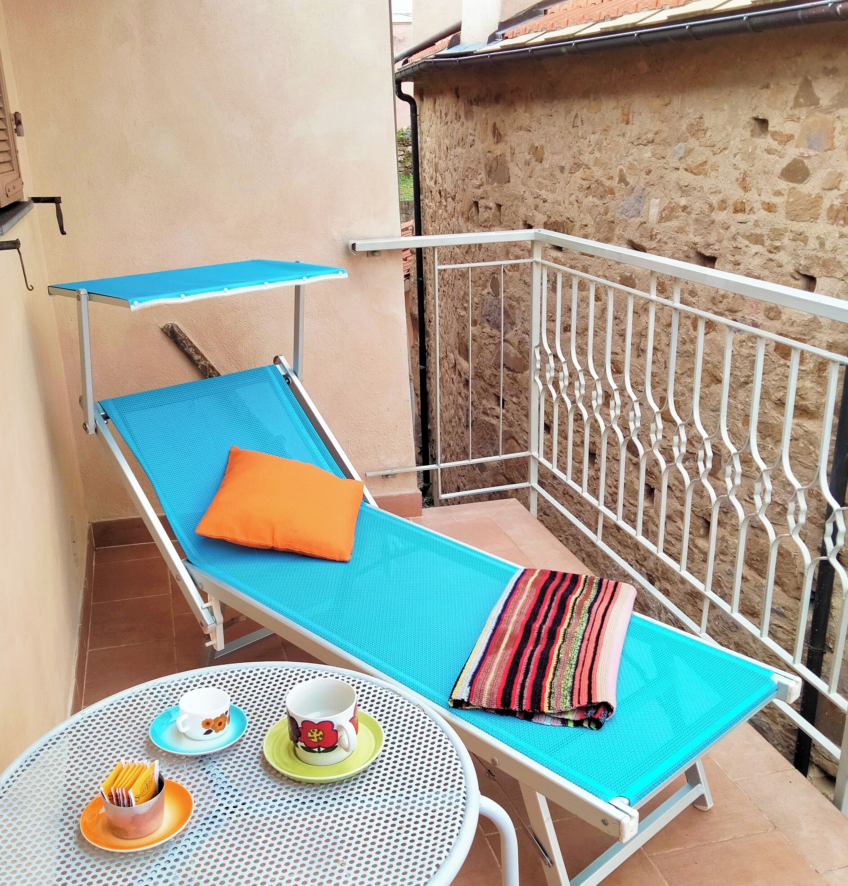 Un balcon avec un fauteuil de jardin bleu, une petite table avec une tasse et une soucoupe, et une serviette à rayures.
