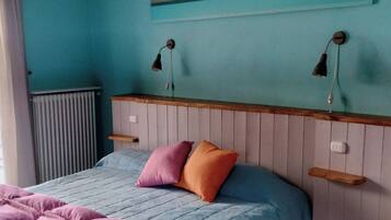 Een slaapkamer met een bed, twee wandlampen, een radiator en een kleurrijk abstract schilderij.