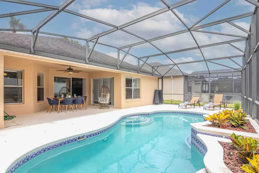 A covered outdoor swimming pool with a glass ceiling, a patio area with chairs, and a small garden.