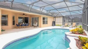 Una piscina exterior cubierta con techo de vidrio, un área de patio con sillas y un pequeño jardín.